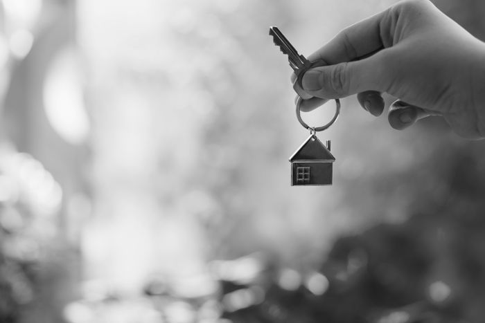 A hand holding a key with a house key-ring.